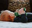 Baby liegt auf dem Rücken und hat ein Spielzeug in der Hand