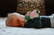 Baby liegt auf dem Rücken und hat ein Spielzeug in der Hand