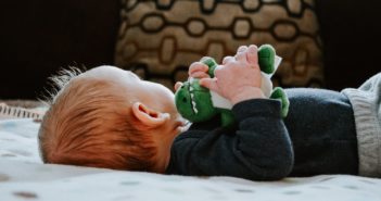 Baby liegt auf dem Rücken und hat ein Spielzeug in der Hand