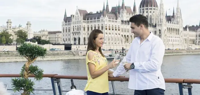 Ein Paar stößt an auf dem Sonnendeck der Primadonna, im Hintergrund das Parlament von Budapest