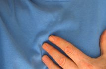 Person in blauem T-Shirt hat Herzschmerzen / Schmerzen in der Brust - Anzeichen auf einen Herzinfarkt