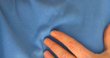 Person in blauem T-Shirt hat Herzschmerzen / Schmerzen in der Brust - Anzeichen auf einen Herzinfarkt