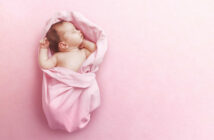 Ein Baby liegt eingekuschelt in eine rosa Decke und schläft.