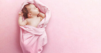 Ein Baby liegt eingekuschelt in eine rosa Decke und schläft.