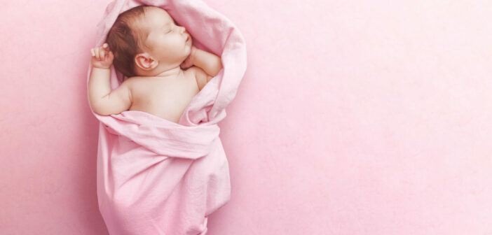 Ein Baby liegt eingekuschelt in eine rosa Decke und schläft.