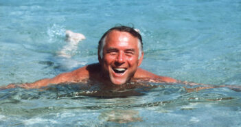 Ein älterer Mann schwimmt lächelnd der Kamera entgegen