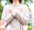 Eine Frau mit einem beigen Pullover steht in einem Garten und hat ihre Arme vor der Brust überkreuzt. Bild: Adobe Stock