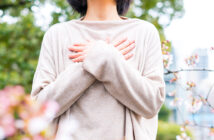Eine Frau mit einem beigen Pullover steht in einem Garten und hat ihre Arme vor der Brust überkreuzt. Bild: Adobe Stock
