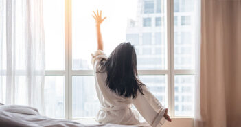 Eine Frau räkelt sich am Morgen kurz nach dem AUfwachen. Durch das Fenster scheint die Sonne herein.