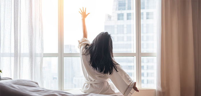 Eine Frau räkelt sich am Morgen kurz nach dem AUfwachen. Durch das Fenster scheint die Sonne herein.