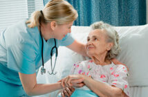 Eine Krankhausbedienstete kümmert sich um eine ältere Frau, die in einem Krankenbett liegt.